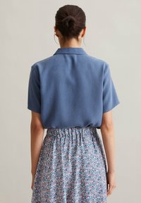 Kurzärmliges blaues Shirt aus glattem Stoff mit Kragen, kombiniert mit einem gemusterten, elastischen Blumenrock in sanften Farben.