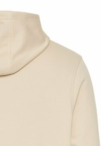 Jasno beżowy hoodie z wysokim kołnierzem, ukazujący tył i część prawego rękawa. Widoczna jest miękka struktura materiału.