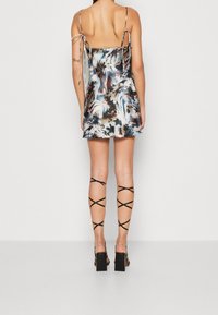 Robe nuisette en satin avec un motif floral en bleu, marron et crème. Elle dispose de fines bretelles ajustables et d'une coupe courte, associée à des talons noirs à lanières.