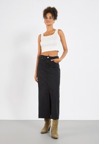 Svart denimskjørt med frontsplitt, høy midje og lommer, paret med en hvit ribbet crop tank topp og beige ankelstøvler.
