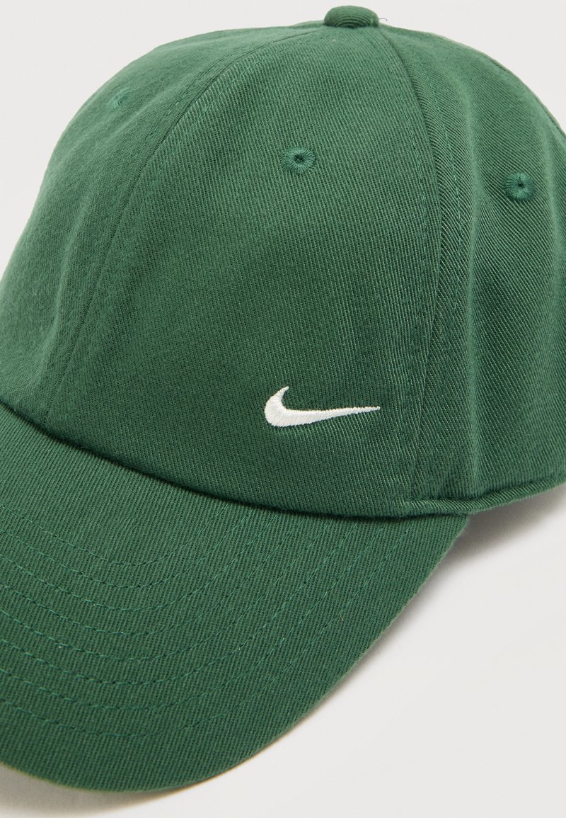 Green baseball cap with white embroidered Nike swoosh logo on front panel, made of ribbed fabric with stitched ventilation eyelets.