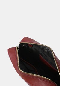 Borsa di pelle rossa scura aperta con zip dorata, che mostra l'interno foderato di tessuto nero e una tasca interna con zip.