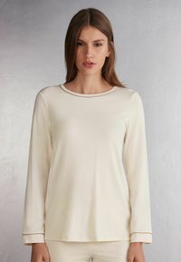 Crèmekleurig top met lange mouwen, ronde halslijn en contrasterende afwerking, gemaakt van een soepele stof, voorzien van een relaxte pasvorm en een minimalistisch ontwerp.
