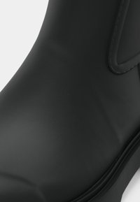 Pogled od blizu na crnu glatku kožnu čizmu, fokus na prst s vidljivim šavovima i zaobljenim rubom đona, na bijeloj pozadini.