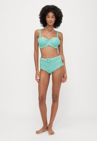 A turquoise, glittery two-piece bikini featuring a structured underwire bra with adjustable straps and high-waisted bottoms with a belt detail.