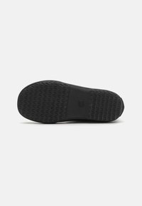 Semelle de chaussure noire avec une texture et un motif antidérapants. La forme est plate et large avec une zone centrale lisse et des bords surélevés.