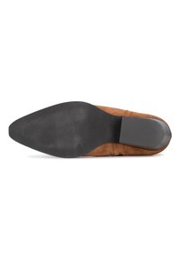Zapato de ante marrón con punta afilada, suela de goma negra lisa y un detalle mínimo. El tacón es bajo y ligeramente redondeado.