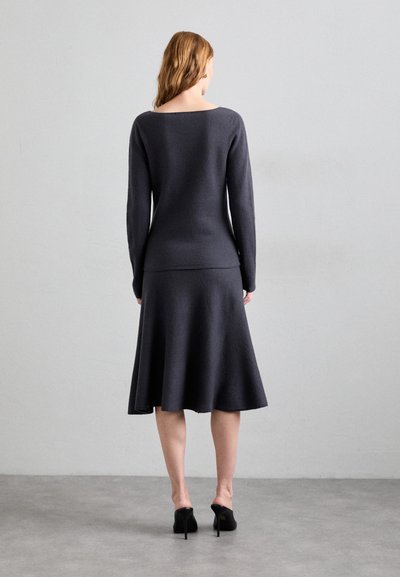 Dunkelgraues langärmeliges Strickoberteil, kombiniert mit einem ausgestellten Rock. Glatte Textur, figurbetonter Oberteil und sanfter Saum, ergänzt durch schwarze High Heels.