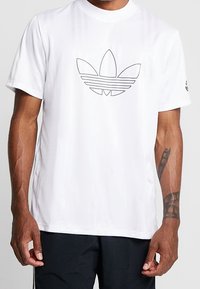 Bílý sportovní tričko vyrobené z prodyšného materiálu, s černě orámovaným logem Adidas umístěným na hrudi. Krátké rukávy a kulatý výstřih.