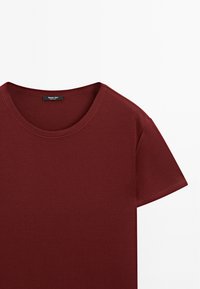Burgundy crew-neck t-shirt made of soft cotton. Short sleeves, smooth texture, and a visible brand label at the neckline.