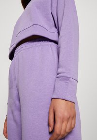 Sudadera recortada morada de corte relajado, con una textura suave y puños acanalados, combinada con pantalones jogger a juego que cuentan con una cintura elástica.