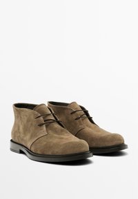 Stivaletti alla caviglia in suede marrone con punta tondeggiante, design minimalista e lacci neri. Soletti in gomma nera spessa con leggero tacco.