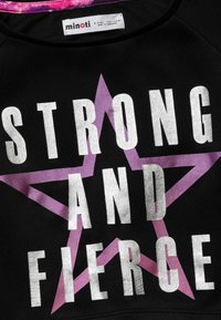 Black sweatshirt featuring bold, silver text "STRONG AND FIERCE" over a purple star design. Label reads "minoti." Soft fabric with a textured finish.