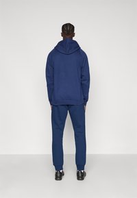 Navy blue cotton hoodie with a large hood, paired with matching sweatpants. Features ribbed cuffs and a relaxed fit. Simple design, no patterns.