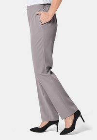 Graue, dehnbare Hosen mit elastischem Bund und seitlichen Taschen. Kombiniert mit schwarzen High Heels, die ein spitzes Design haben.