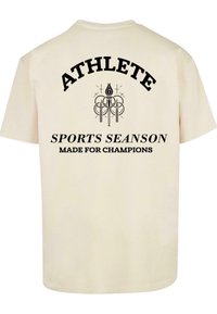 Krēmkrāsas kokvilnas T-krekls īsām piedurknēm ar melnu tekstu "ATHLETE" virs "SPORTS SEASON" un "MADE FOR CHAMPIONS" aizmugurē.