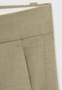 Ljusbeige tygmapp med en texturerad yta. Har en synlig söm och sydda detaljer, med en öppen flik upptill.