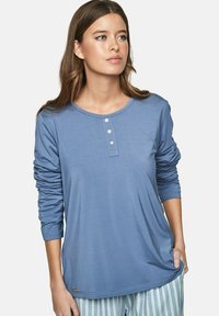 T-shirt à manches longues bleu fabriqué en tissu doux, avec un col rond et une patte de boutonnage à trois boutons, présentant des manches retroussées et une coupe décontractée.