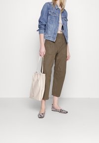 Jeansjacka, beige topp, olivgröna byxor och skor med ormskinnsmönster. Ljus färgad väska med justerbar axelrem. Neutral färgskala.