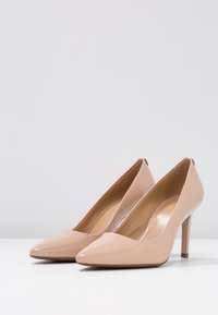 Escarpins beige en cuir verni à talons hauts, avec un bout pointu, un design épuré et une finition lisse. Idéaux pour des occasions formelles ou professionnelles.