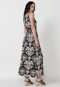 Robe maxi en noir et crème avec un motif floral, sans manches et avec une taille texturée. Assortie à des sandales à talons compensés noires.
