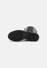 Schwarze Gummisohle mit einem strukturierten Muster für Grip. Das Obermaterial besteht aus einer Mischung grauer Materialien und hat ein rundes Zehen-Design.