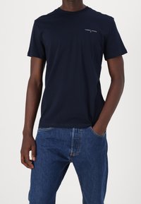 Granatowy bawełniany t-shirt z krótkimi rękawami i okrągłym dekoltem, z małym białym logo "TOMMY JEANS" na lewej piersi.