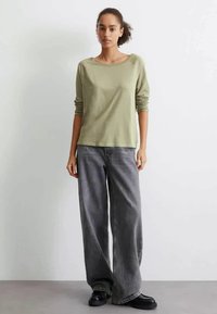 Světle zelený top s dlouhým rukávem a uvolněným střihem, kombinovaný s šedými širokými džínami a černými robustními botami. Jednoduchý design, jemná textura.