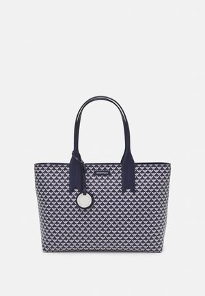 Sac tote bleu marine avec un motif répétitif de logos d'aigle blanc, deux poignées, et un pendentif argenté rond suspendu près du centre supérieur.
