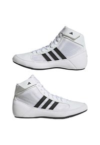 Baskets montantes blanches avec des bandes noires, des empiècements en mesh, des lacets et un logo sur le col de la cheville, vues de côté sur fond blanc.