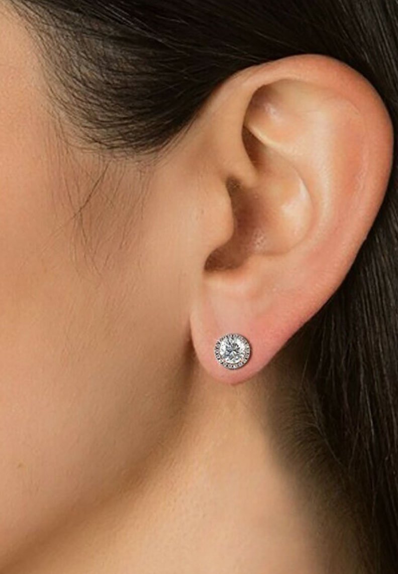 Orecchini a bottone rotondi in argento con un grande cristallo trasparente al centro, circondato da piccole pietre di strass. Finitura metallica liscia, design classico.