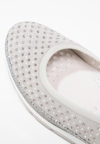 Chaussure gris clair à enfiler avec de petits points brillants et une bordure argentée texturée le long du bord de la semelle.