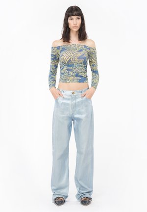 Top blu e giallo con fantasia, scollato e con maniche lunghe, abbinato a jeans ampi di colore blu metallici chiaro. Tessuti texture e finitura liscia.