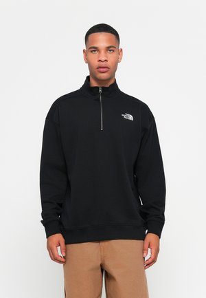Pullover in pile nero con colletto alto e zip a un quarto. Presenta un piccolo logo bianco sul lato sinistro del petto e polsini a coste.