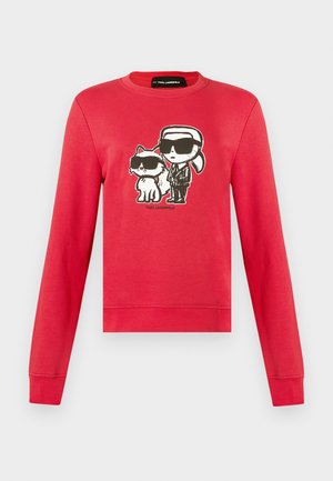 Sweat-shirt rouge à manches longues avec un dessin animé d'une personne avec une queue de cheval et un chat, tous deux portant des lunettes de soleil noires, avec le texte "Karl Lagerfeld" en dessous.