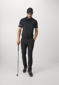 Black polo shirt with three-striped sleeves, black pants, and black athletic shoes. Holding a golf club, wearing a matching cap.