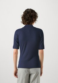 Marineblå ribbestrikket topp med høy krage og korte ermer, parret med lysegrå mønstrede bukser. Glatt tekstur, tettsittende design.