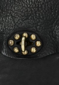 Chiusura della borsa a mano in pelle nera caratterizzata da un anello metallico centrale circondato da borchie decorative in tono oro. Superficie strutturata con grana visibile.