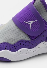 Fialové a šedé tenisky s texturovaným svrškem, širokým páskem a bílou mezipodešví s černými skvrnami. Obsahují detail s logem.