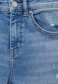 Tissu en denim bleu clair présentant un design à cinq poches, des surpiqûres visibles en orange et des détails légèrement usés sur le devant.