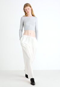Gray cropped long-sleeve top paired with white, loose-fitting pants and black ankle boots. Simple design with an elastic waistband on pants.