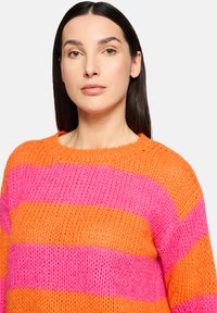Pull en tricot avec de larges rayures horizontales orange et rose, col rond et finition texturée.