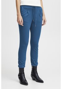 Blå joggerbyxor i mjukt material, med tapered passform, elastisk midja med dragsko och sidofickor. Matchas med svarta ankelstövlar.