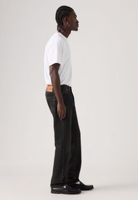 Μαύρο τζιν με ίσια γραμμή, που διαθέτει ένα ανοιχτό καφέ δερμάτινο ταμπελάκι στη πίσω ζώνη μέσης, συνδυασμένο με λευκό απλό μπλουζάκι.