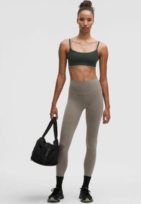 Sujetador deportivo verde oscuro y leggings de talle alto marrón claro, con un bolso de gimnasio negro. Presenta un diseño ajustado y una textura suave.