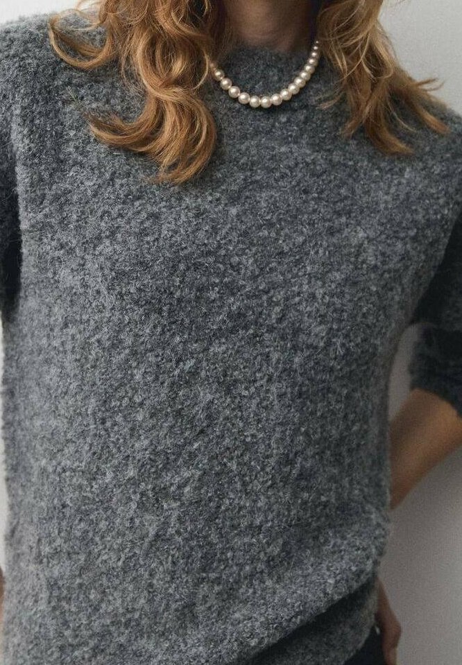 Pull gris en maille texturée avec un col rond et des manches trois-quarts, accompagné d'un collier de perles. Matière douce et confortable.