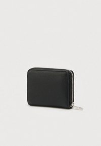 Cartera negra de cuero texturizado con cremallera plateada y pestaña de tirador, mostrada cerrada sobre un fondo claro.