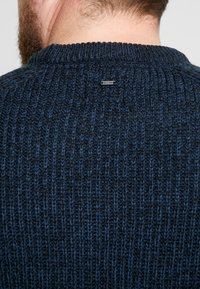 Maglione lavorato a maglia di colore blu navy con texture a costine, dotato di scollatura rotonda e di un piccolo etichetta metallica del marchio sul retro.