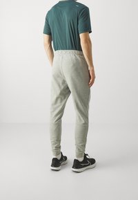 Pantalones jogger grises con cinturilla elástica, piernas ajustadas y bolsillos laterales. Combinados con una camiseta de manga corta verde oscura y zapatillas negras.