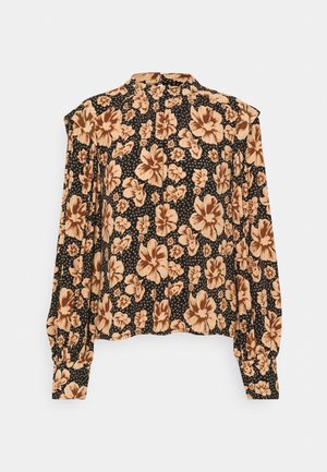 Blouse noire à manches longues avec motif floral beige, col montant, épaules structurées et poignets boutonnés.